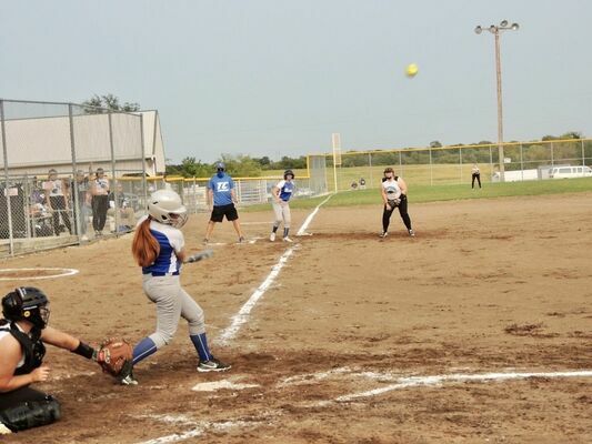 Anissa Williams smacks the ball, while Lexi Wyant waits to score from third.